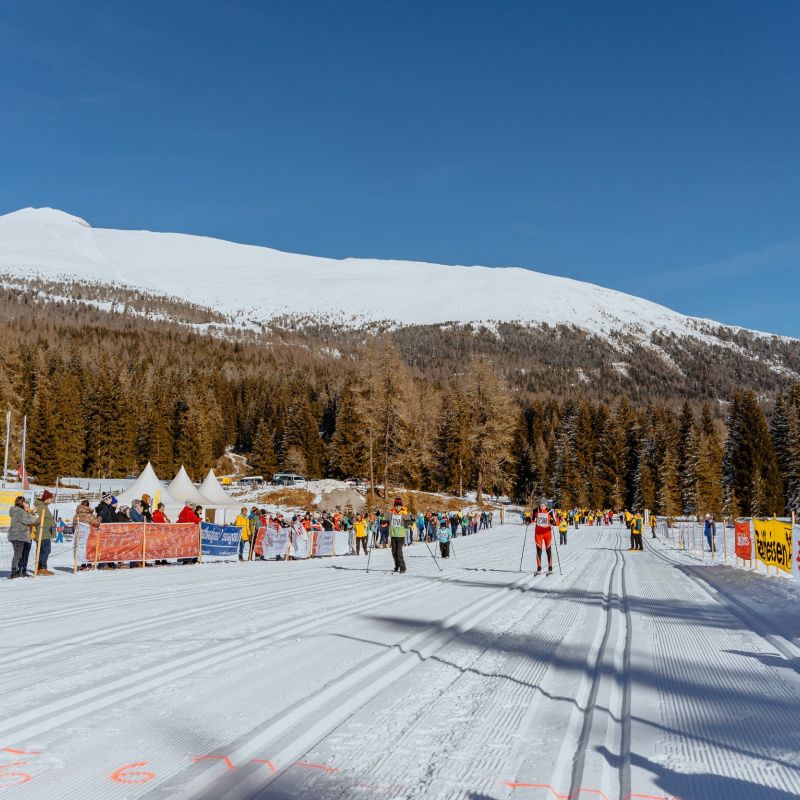 Skilangläufer auf präparierter Loipe im Salzburger Lungau, umgeben von schneebedeckten Bergen und Wäldern unter blauem Himmel.