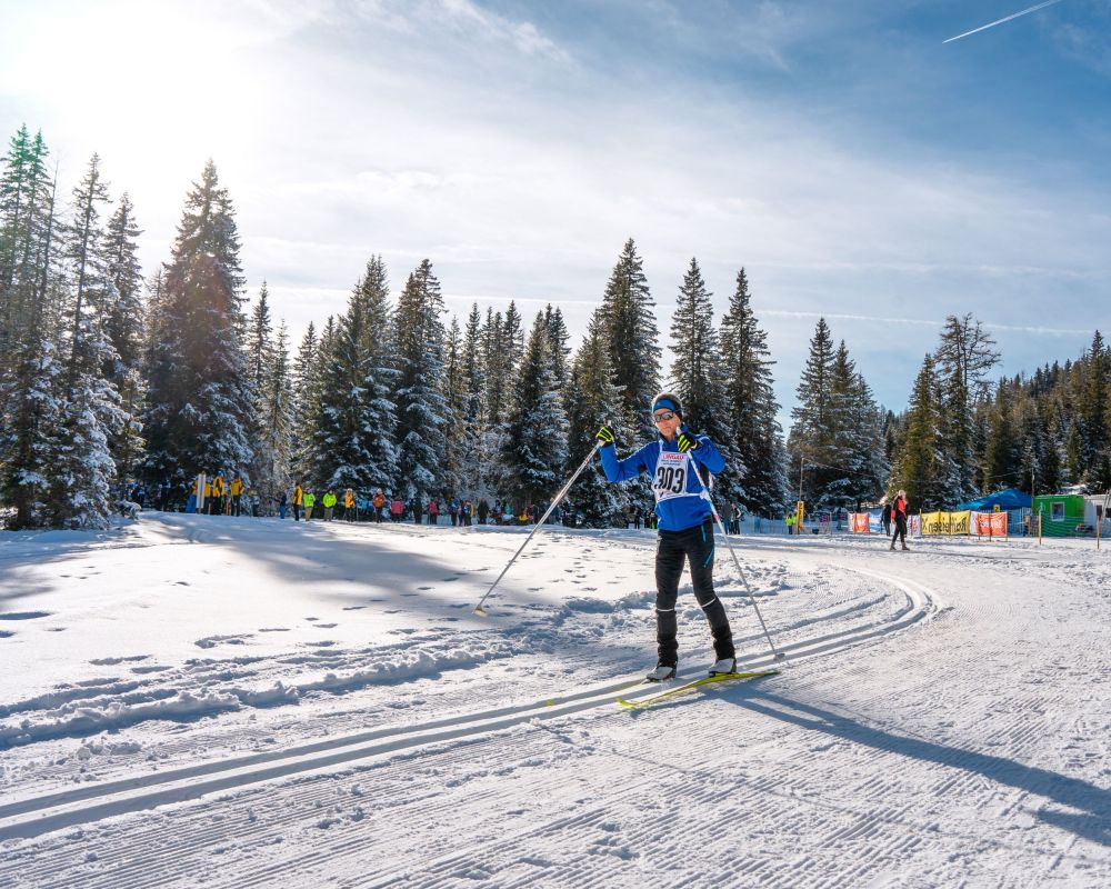 Skilangläufer auf verschneiter Strecke im Salzburger Lungau, umgeben von schneebedeckten Bäumen und Zuschauern im Hintergrund.