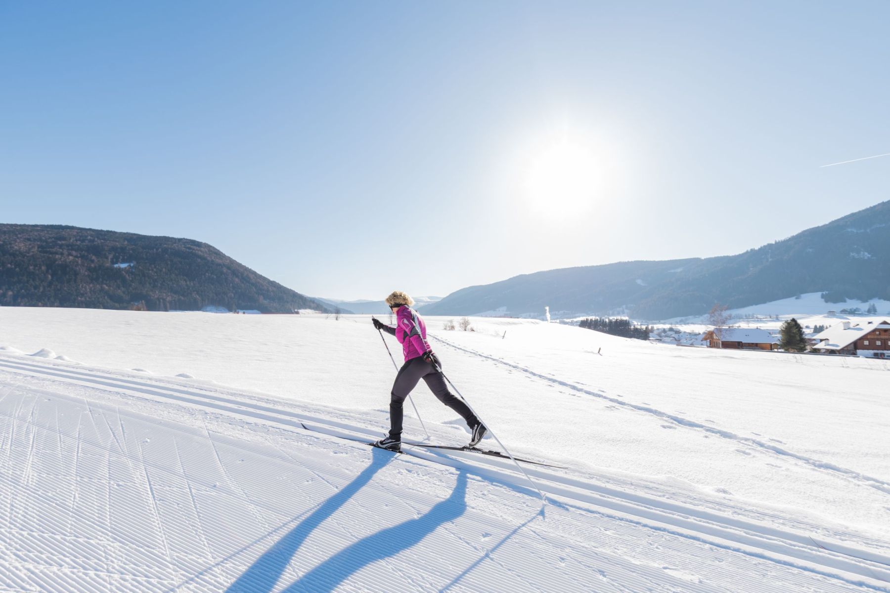 Person beim Langlaufen auf verschneiter Ebene im Salzburger Lungau, sonniger Himmel, Berge im Hintergrund.