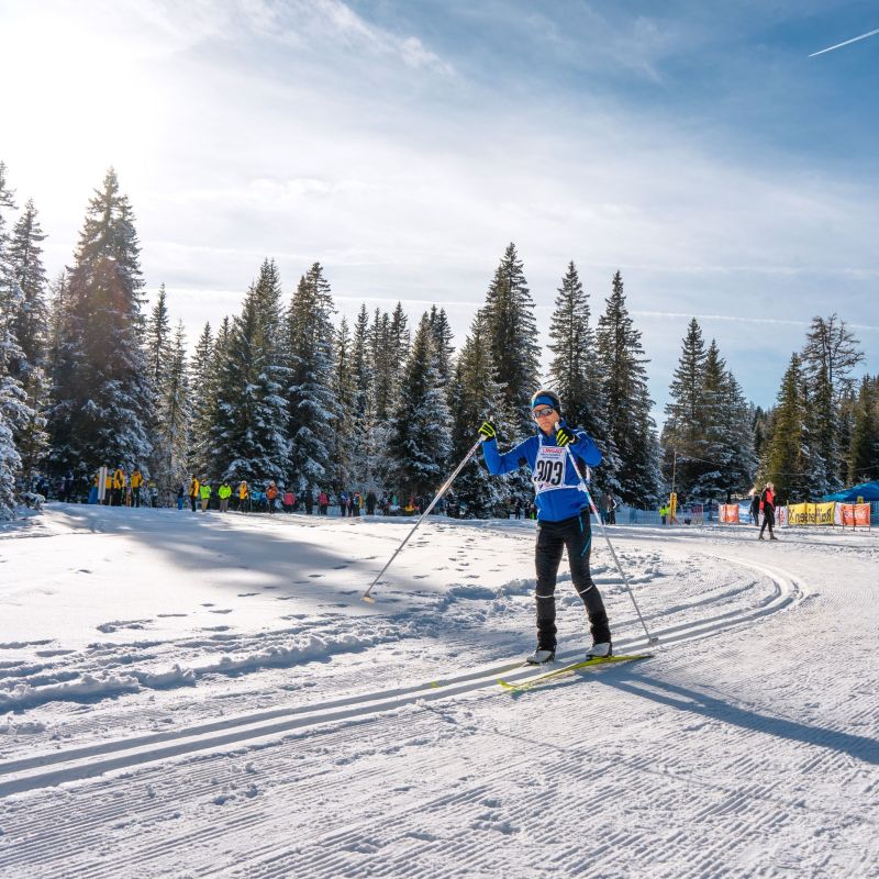 Skilangläufer auf verschneiter Strecke im Salzburger Lungau, umgeben von schneebedeckten Bäumen und Zuschauern im Hintergrund.