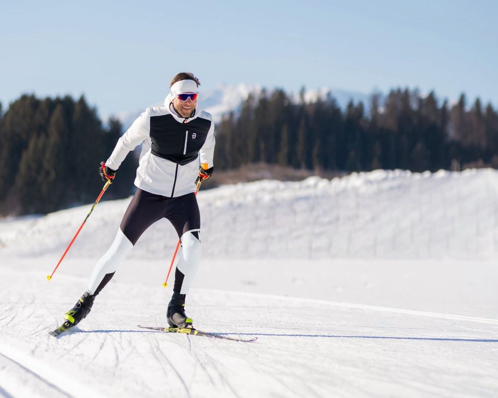 Person beim Skilanglauf auf verschneitem Feld im Salzburger Lungau, blauer Himmel, Wald im Hintergrund.