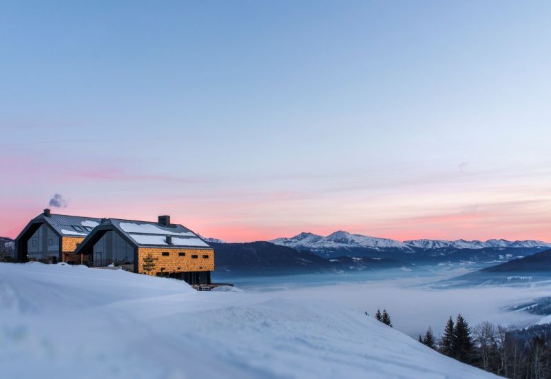 Holzhaus im Schnee, Salzburger Lungau, Abenddämmerung, Berge im Hintergrund, rosa Himmel.