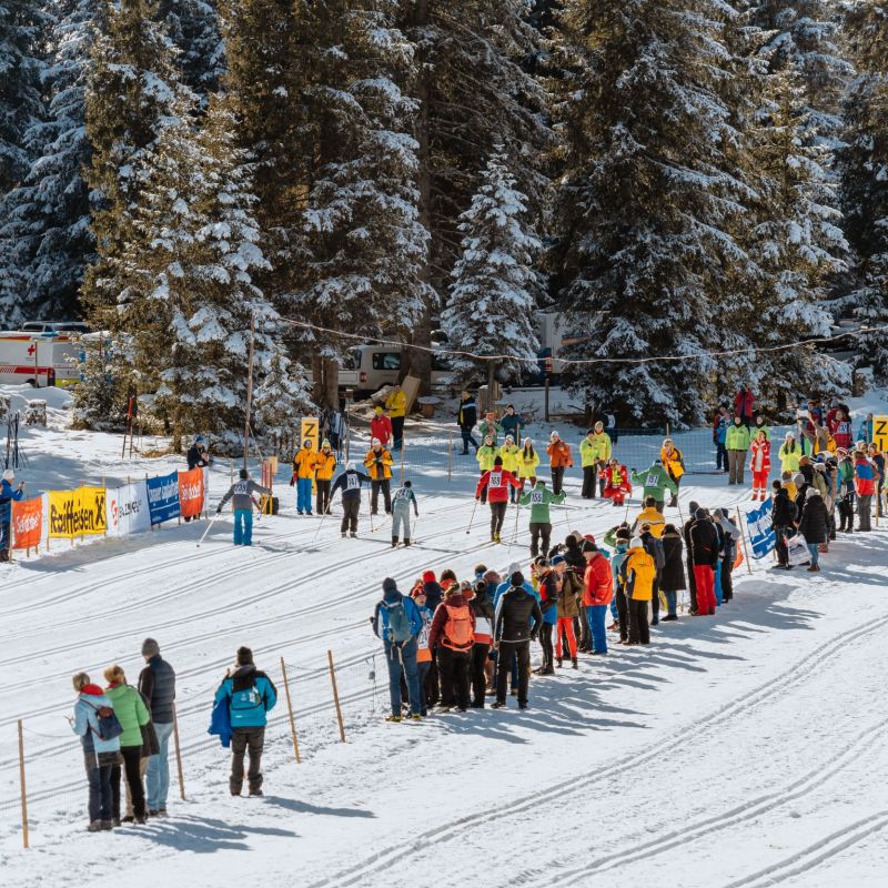 Skilanglauf-Wettbewerb im verschneiten Salzburger Lungau. Zuschauer und Teilnehmer stehen neben Loipen, umgeben von schneebedeckten Bäumen.
