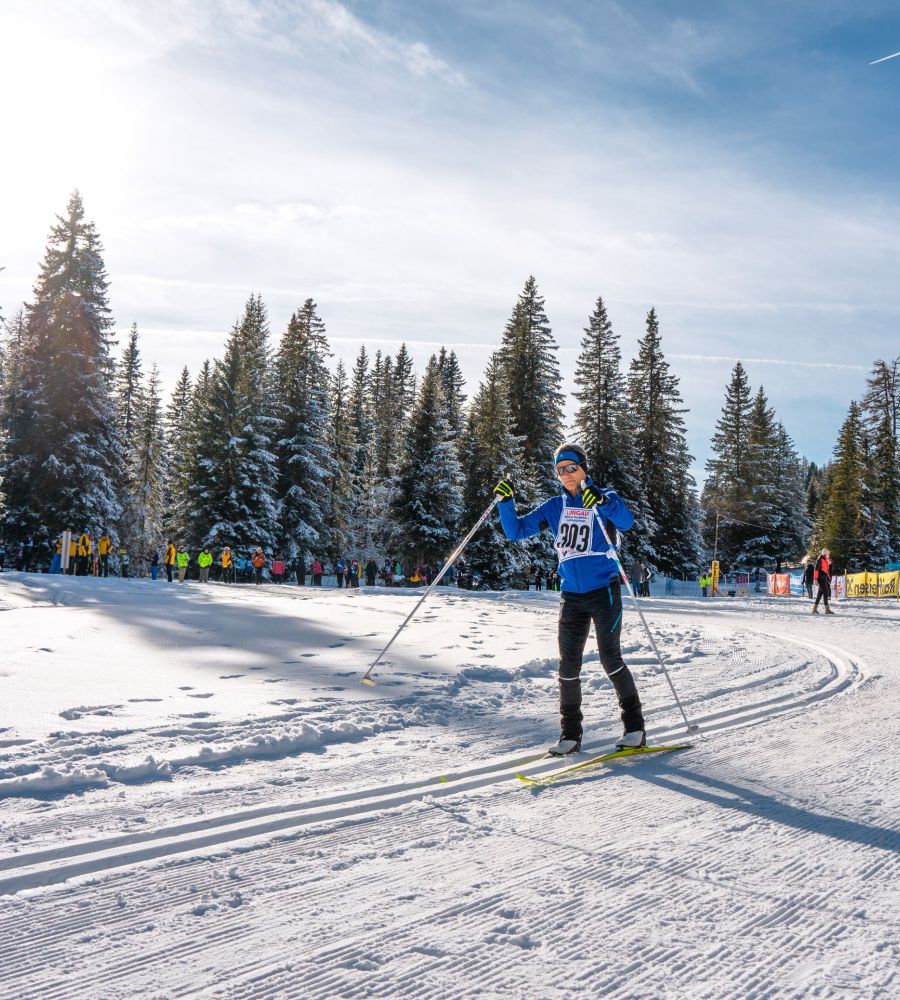 Skilangläufer auf verschneiter Strecke im Salzburger Lungau, umgeben von schneebedeckten Bäumen und Zuschauern im Hintergrund.