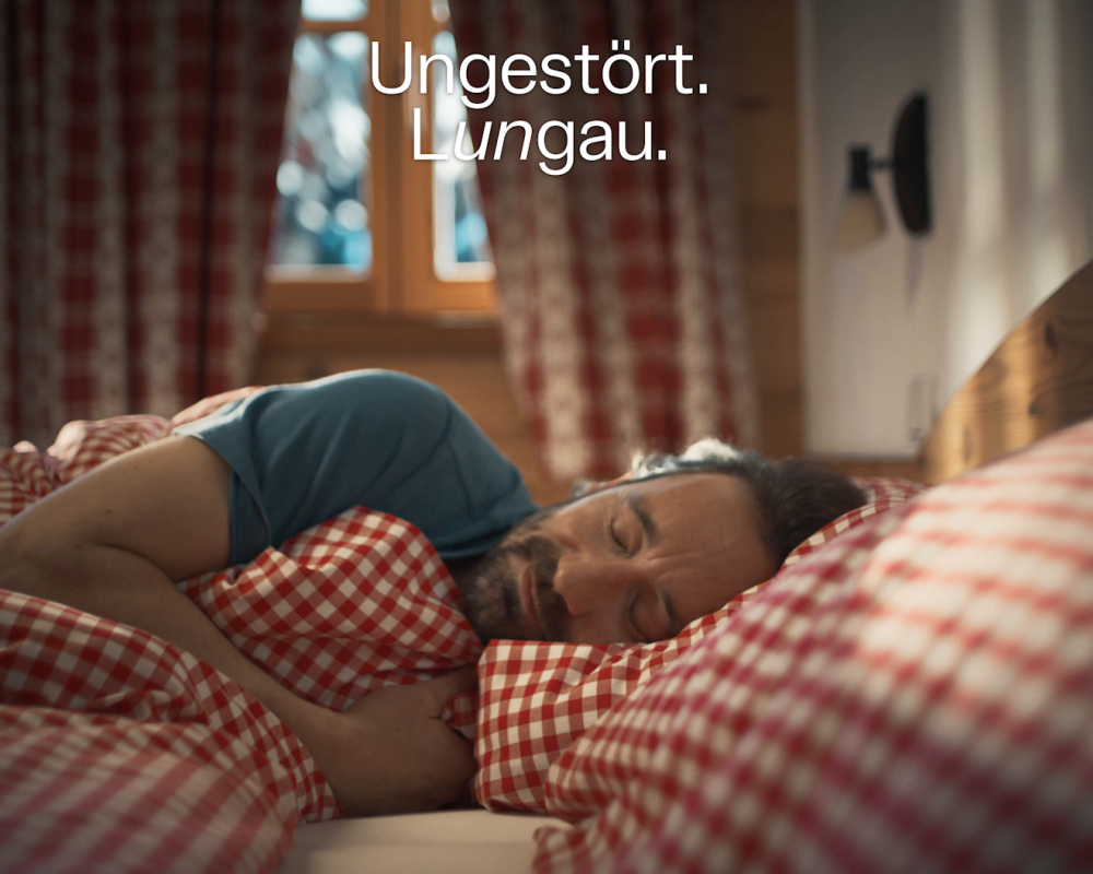 Mann schläft friedlich in kariertem Bettzeug, Fenster mit Vorhängen im Hintergrund, Text: "Ungestört. Lungau."