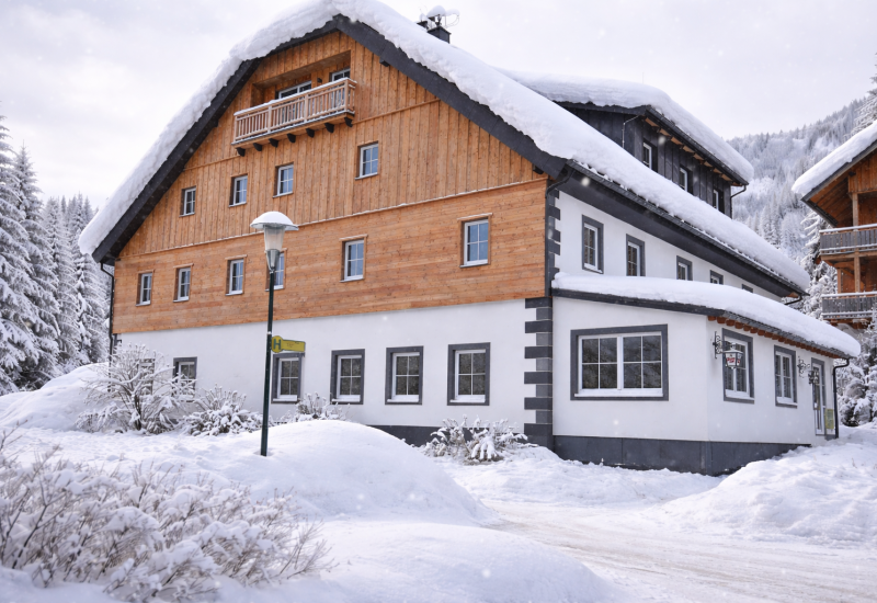 Schneebedecktes Holzhaus im Salzburger Lungau, umgeben von verschneiten Bäumen und winterlicher Landschaft.