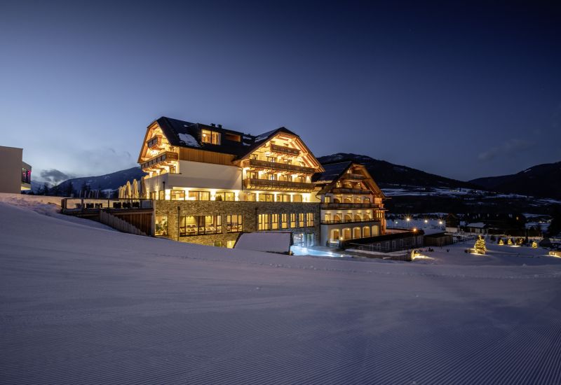 Beleuchtetes Hotel im Salzburger Lungau im Winter, umgeben von schneebedeckten Bergen und beleuchteten Bäumen bei Dämmerung.