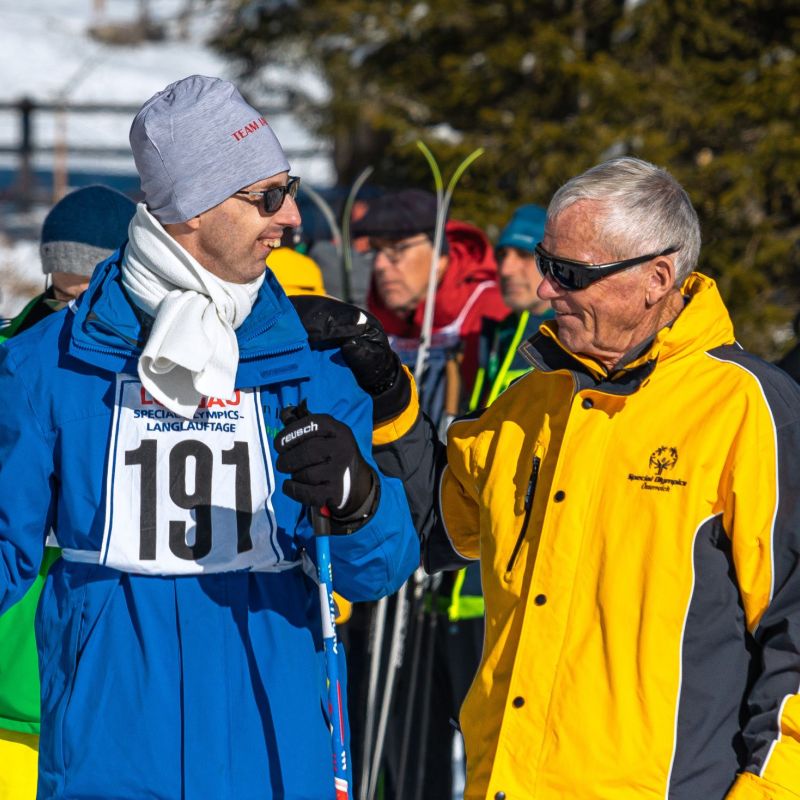 Menschen in Winterkleidung bei einem Skievent im Salzburger Lungau, zwei Personen im Vordergrund unterhalten sich.